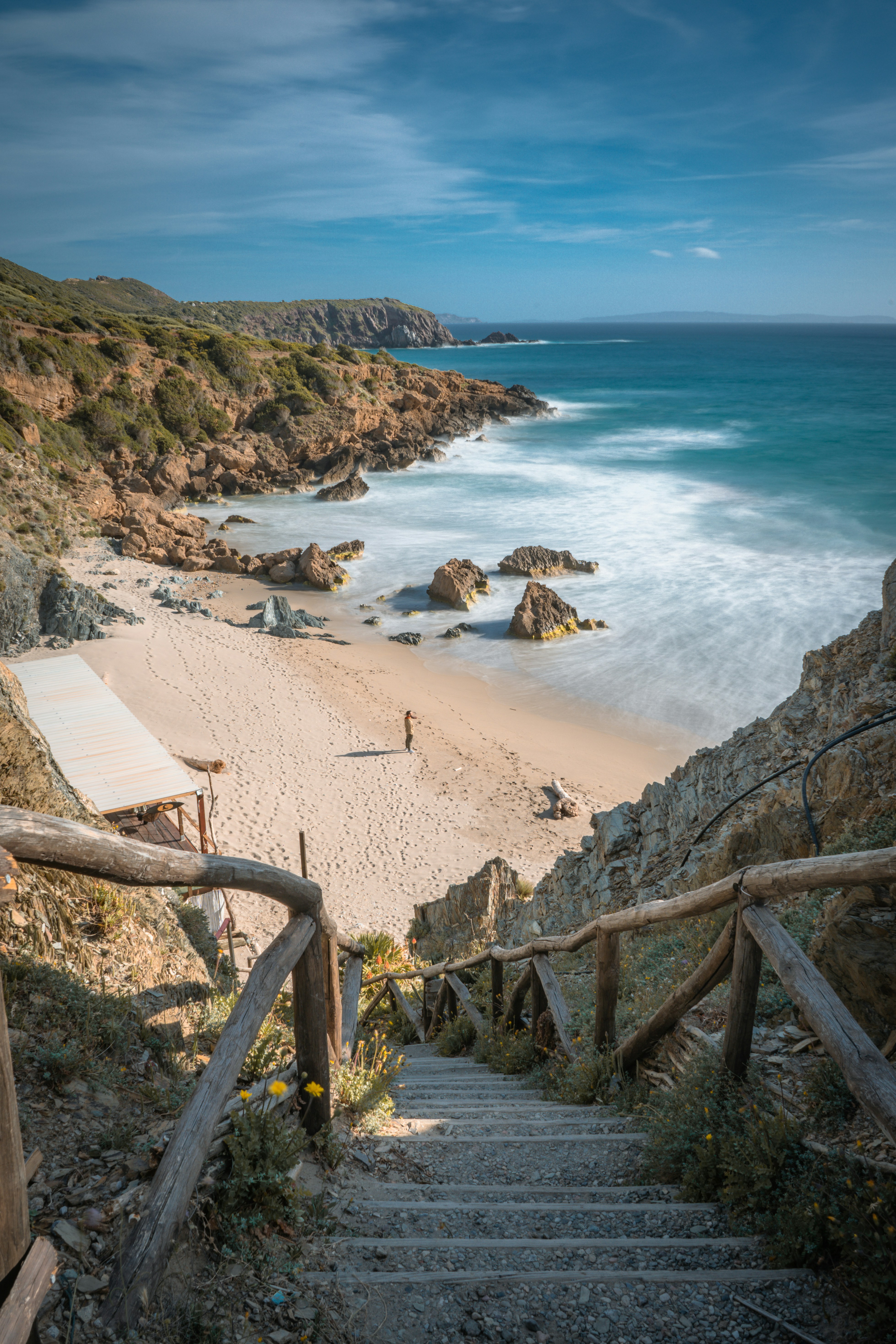 Steps lead down to a sandy beach with rocky coastline.
