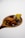 A wooden spoon holds a dark sauce with a glossy texture, along with a yellowish-green food item topped with a small purple flower.
