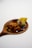 A wooden spoon holds a dark sauce with a glossy texture, along with a yellowish-green food item topped with a small purple flower.