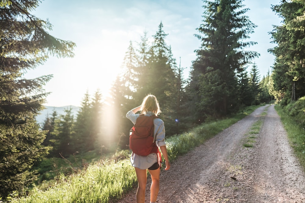 a woman with a backpack walking down a dirt road