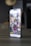 A smartphone displaying an Instagram profile with several thumbnail images on its screen, showing various lifestyle and technology-related pictures. The phone is placed on a tabletop in a dimly lit room with blurred background elements.