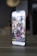 A smartphone displaying an Instagram profile with several thumbnail images on its screen, showing various lifestyle and technology-related pictures. The phone is placed on a tabletop in a dimly lit room with blurred background elements.