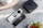 A minimalistic setup with a black streaming device with a logo on top placed on a marble surface. Two sleek, modern remote controls with various buttons are beside it. The arrangement is complemented by decorative plant pots, adding a touch of nature to the scene.