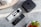 A minimalistic setup with a black streaming device with a logo on top placed on a marble surface. Two sleek, modern remote controls with various buttons are beside it. The arrangement is complemented by decorative plant pots, adding a touch of nature to the scene.