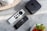 A minimalistic setup with a black streaming device with a logo on top placed on a marble surface. Two sleek, modern remote controls with various buttons are beside it. The arrangement is complemented by decorative plant pots, adding a touch of nature to the scene.