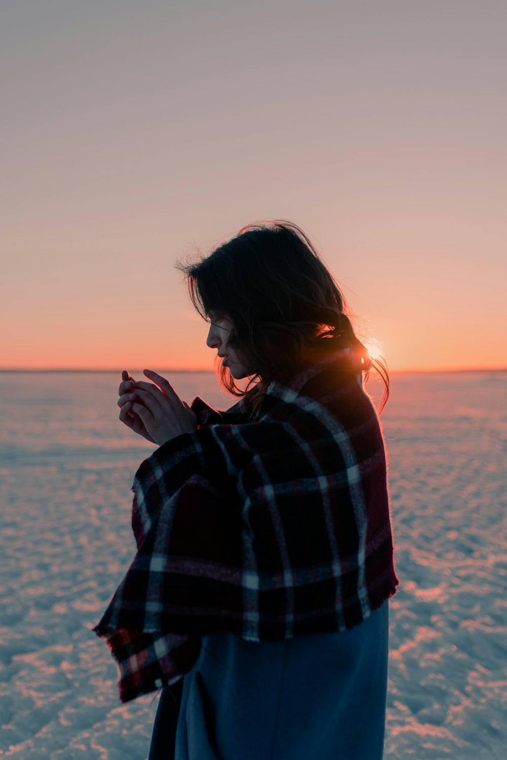 a woman standing in the snow at sunset