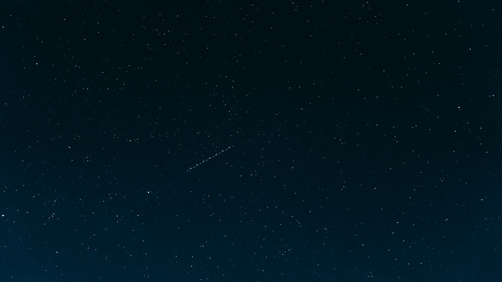 a night sky with stars and a plane in the distance