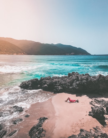 Happy traveler relaxing on a sunny beach with clear blue water in the background.