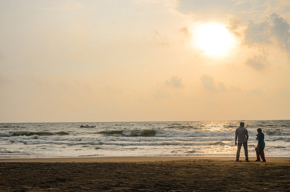 a couple of people standing on top of a sandy beach