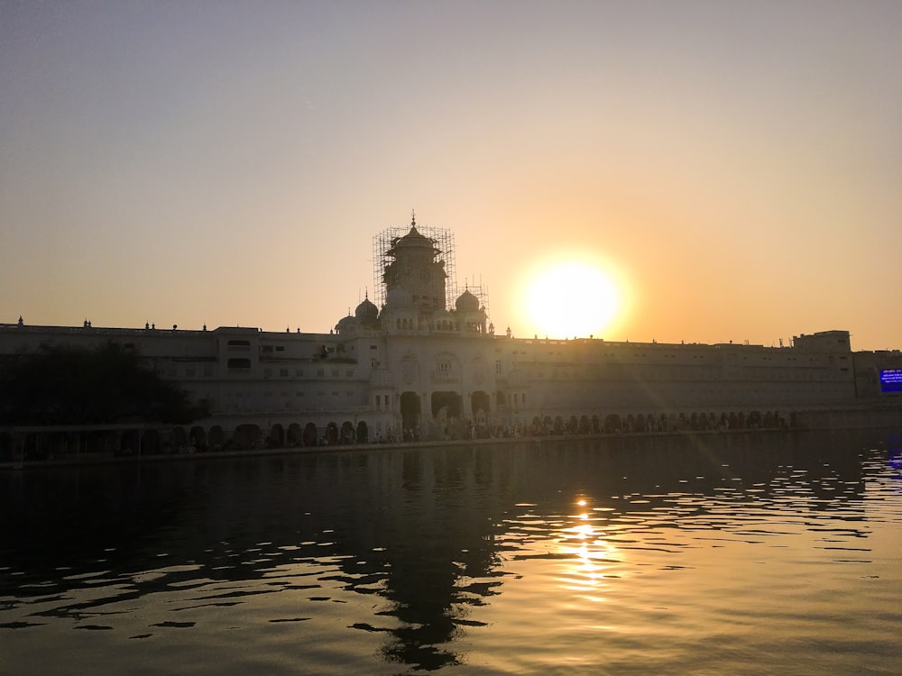 the sun is setting over the water in front of a building