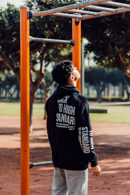 A boy in a cozy hoodie and cargo pants climbing on playground equipment on a crisp autumn day.