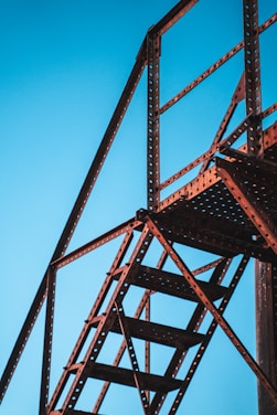 A metal structure framing the sky with stair-like features, characterized by industrial design with holes in the metal beams creating a patterned texture. The structure appears sturdy and functional, intersecting at various angles.