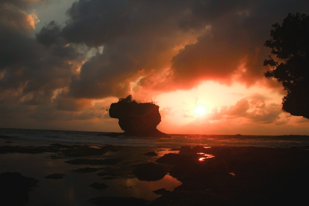 the sun is setting behind a rock formation on the beach