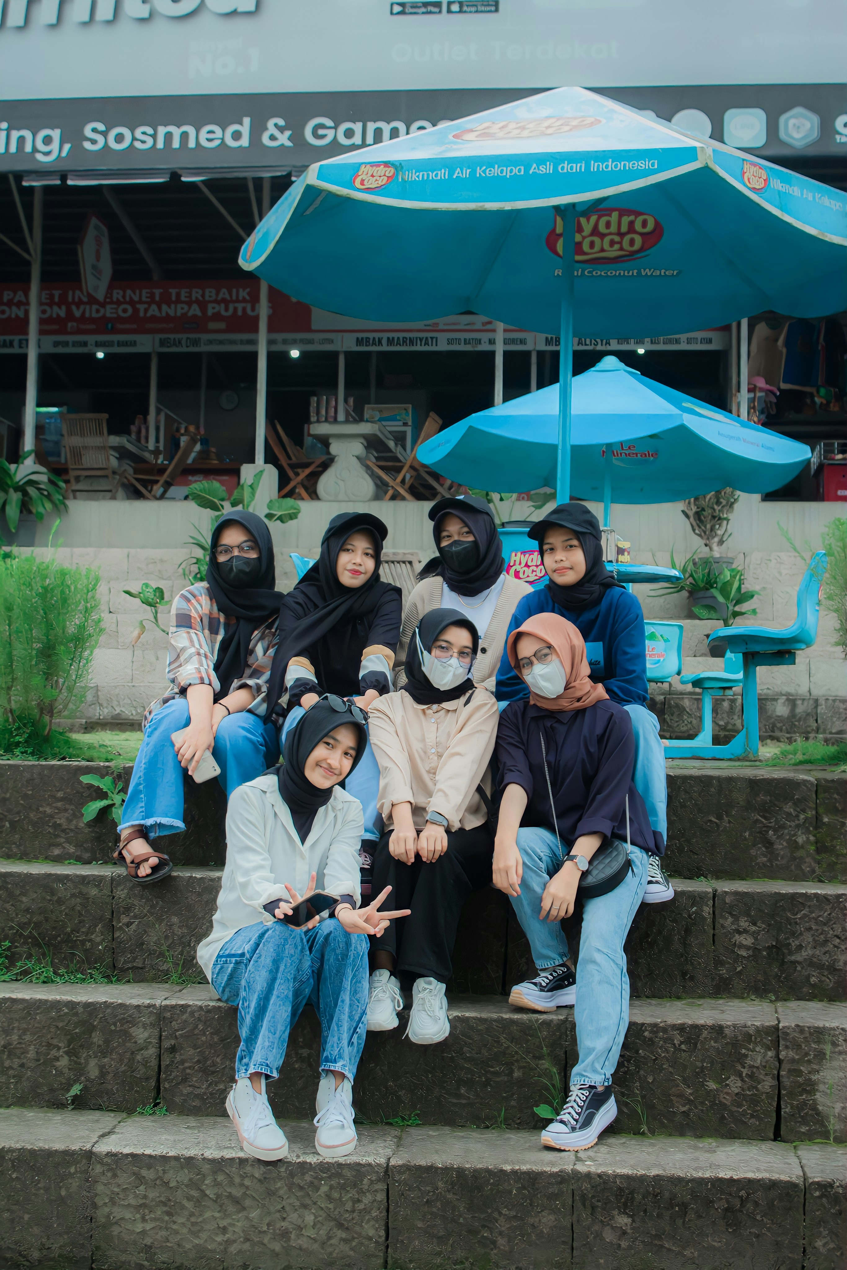 a group of people sitting on steps under a blue umbrella