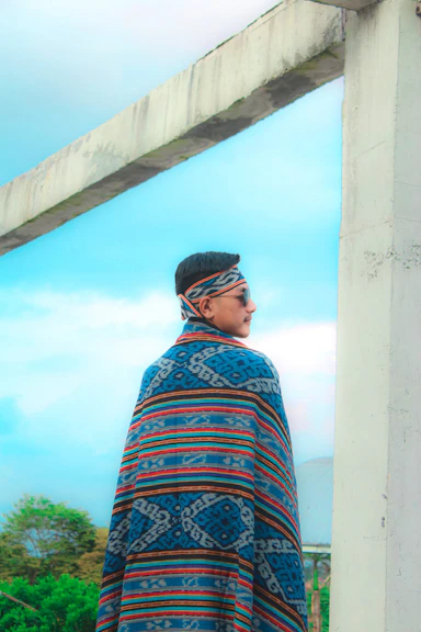 a man in a colorful shawl looking out a window