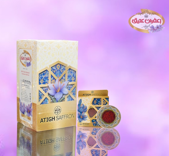 A saffron packaging design featuring a large rectangular box and a smaller round container. The background is a soft gradient of pinks and purples. The packaging is adorned with floral imagery and intricate geometric patterns in shades of blue and gold. The brand name 'ATIGH SAFFRON' is prominently displayed along with a decorative logo.