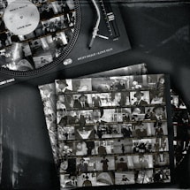 A vintage-style image features a vinyl record player with a record labeled 'Ricky Rique - Love Gun' on the turntable. Nearby, there are film contact sheets displaying black-and-white images of people, including individuals in suits and hats, evoking a classic or retro feel.