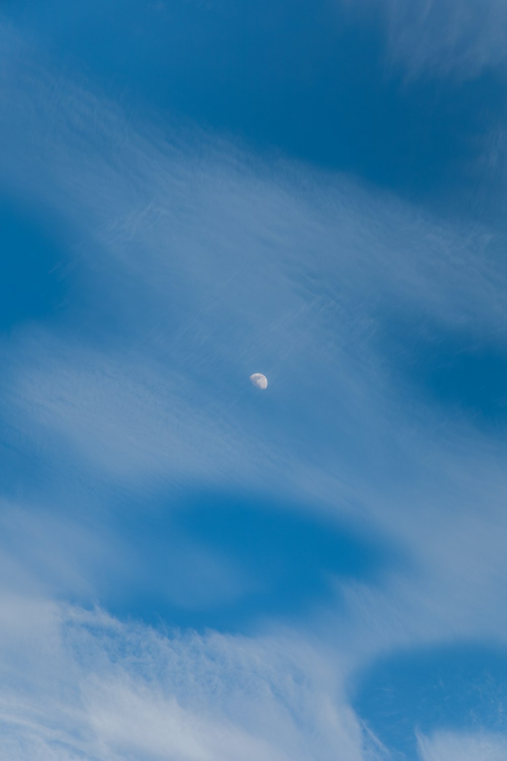 a clear blue sky with clouds and a half moon