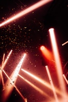 Bright spotlights shine through the air, creating dynamic beams of light against a smoky backdrop. Confetti is scattered throughout the scene, adding to the festive and energetic atmosphere.