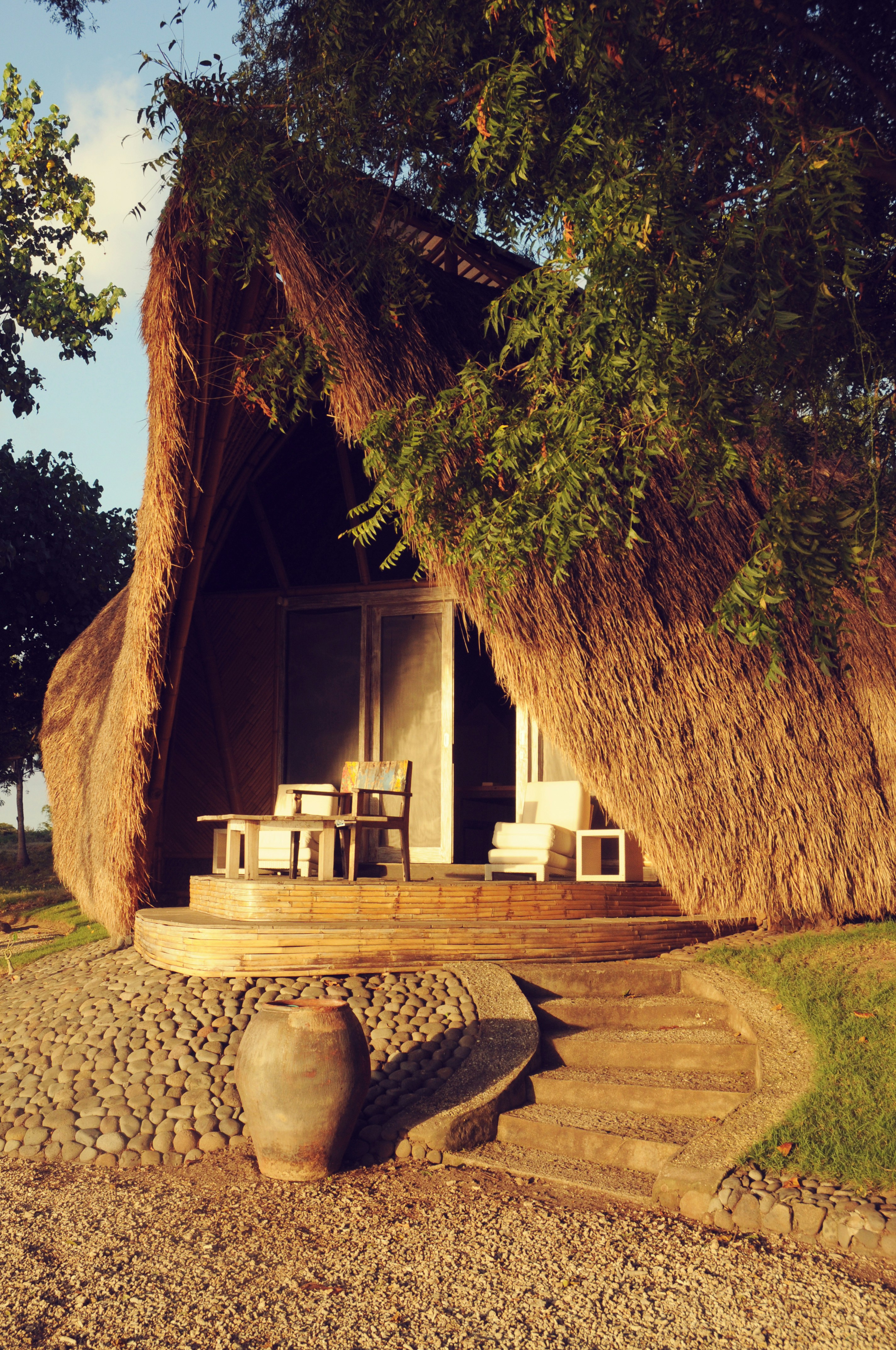 a thatched hut with a table and chairs under a tree