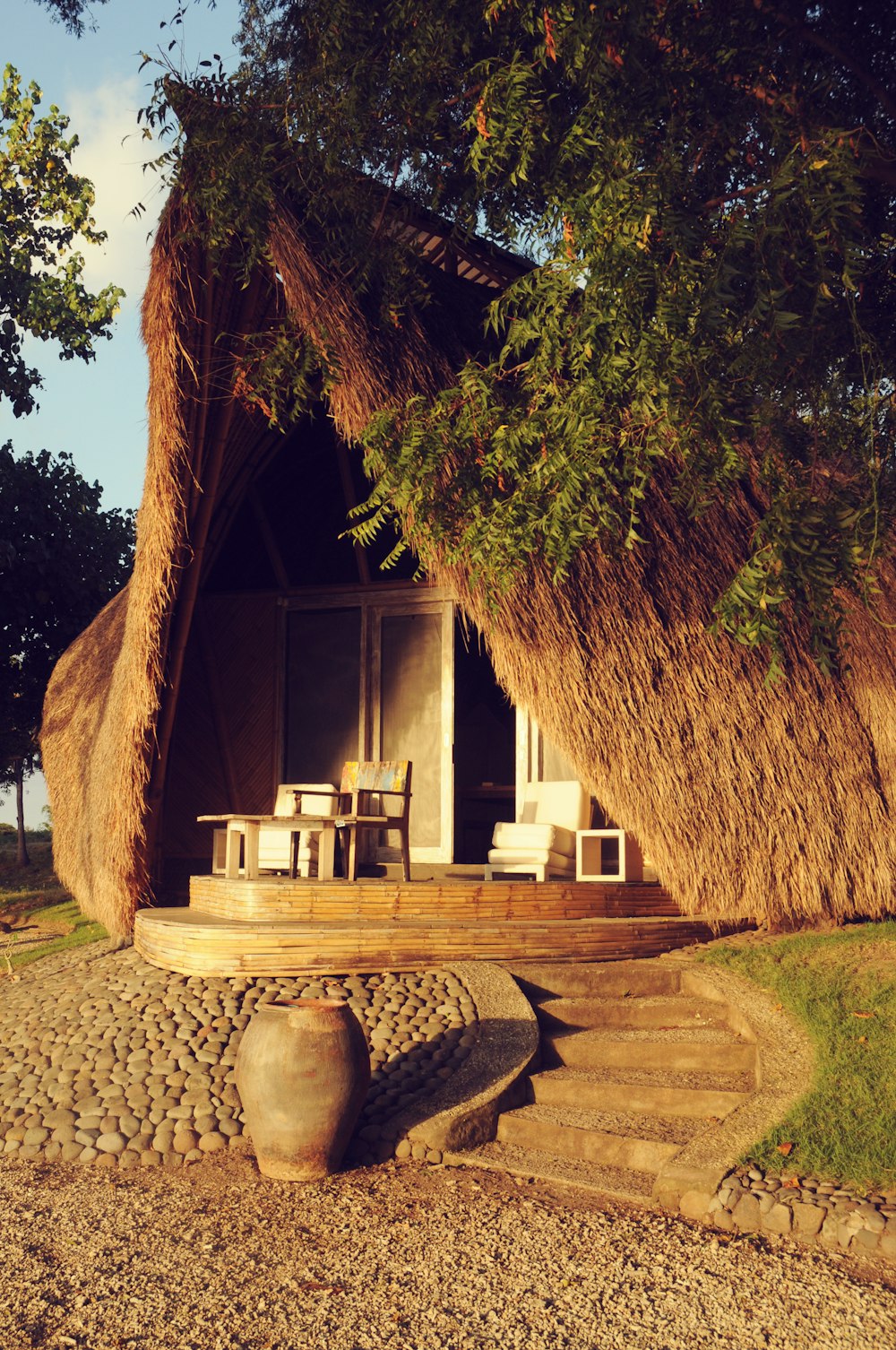 eine strohgedeckte Hütte mit Tisch und Stühlen unter einem Baum