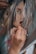 A hand is holding a brush, carefully painting the details on a portrait. The image captures the close-up of the hand in the act of painting, focusing on the delicate brush strokes being added to the lips and face of the portrait. The artwork appears to depict an expressive face with abstract and loose brushwork.