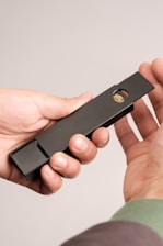 A close-up image of hands holding a sleek, black rectangular object with a small circular compartment containing a green substance.