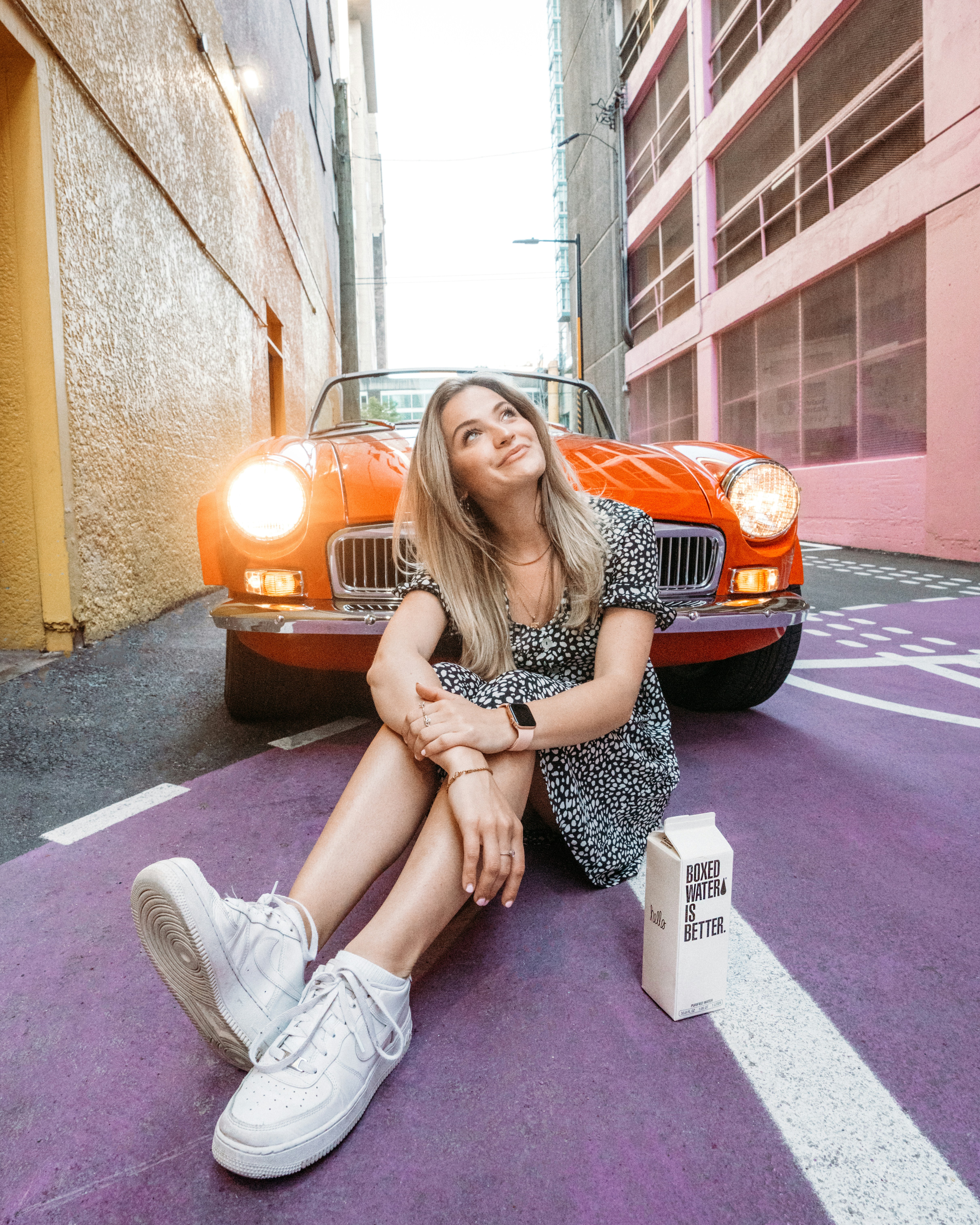 a woman sitting on the ground next to a red car