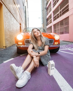 a woman sitting on the ground next to a red car