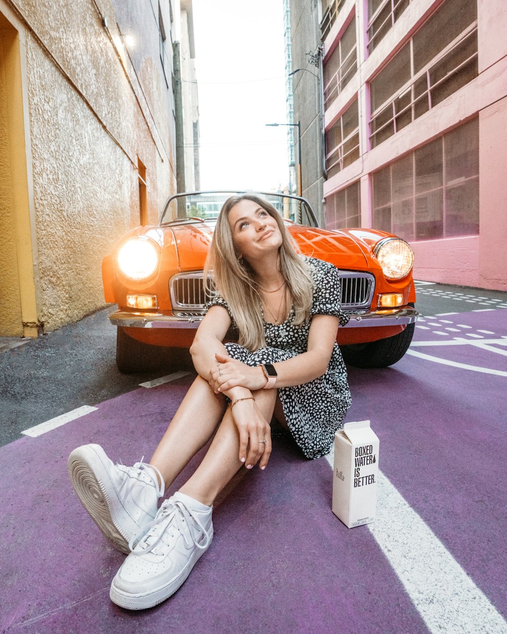 a woman sitting on the ground next to a red car