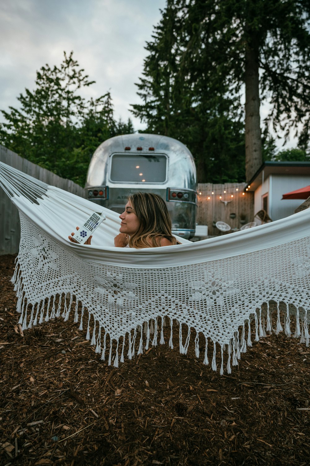 a woman sitting in a hammock with a trailer in the background