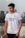 A person is standing outdoors wearing a white sports jersey with blue and orange accents. The jersey has brand logos and text on it. The background suggests an urban setting with buildings and a cloudy sky.