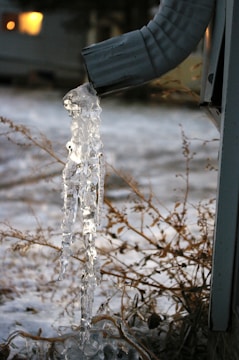 Black seamless gutters installed on a white building with snow melting off the roof in Lander, Wyoming.
