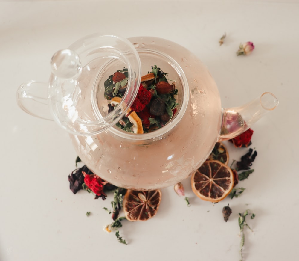a tea pot filled with flowers and fruit