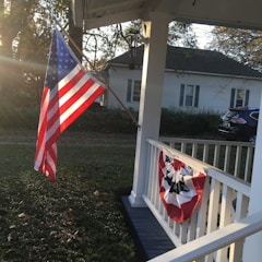 A welcoming front porch of a modern, accessible home with a veteran's flag gently waving nearby.