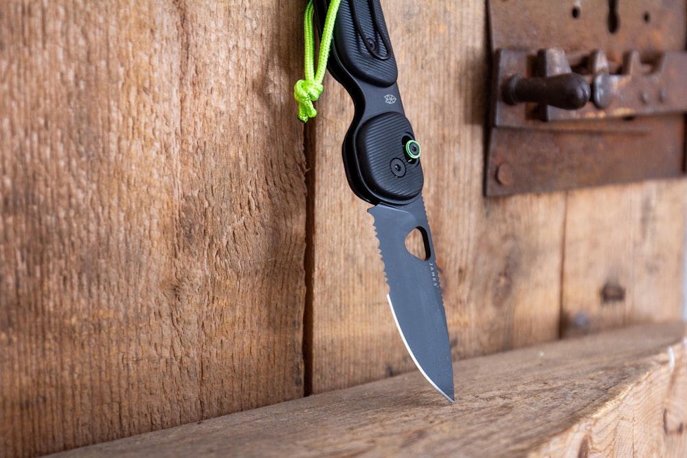 a knife hanging on a wooden wall with a green cord