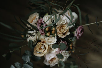Close-up of a luxurious bouquet featuring cream roses and eucalyptus leaves against a soft charcoal background