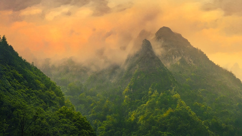 a mountain covered in green trees under a cloudy sky