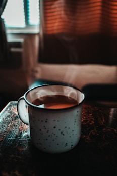 A cozy scene featuring a ceramic-style insulated mug filled with steaming coffee.