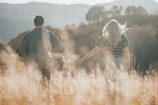 A candid shot of a couple walking hand-in-hand through a sunlit field with charcoal shadows.