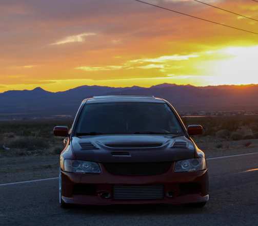 A sleek luxury car parked at a desert resort entrance during sunset.