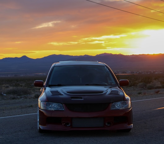 A sleek sedan from Aasra Cab Tours and Travels parked by a scenic mountain road at sunset.