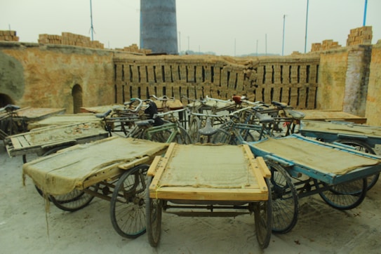 Several three-wheeled carts are arranged in a circular pattern in an open area with stacks of bricks lining the walls. The carts have wooden platforms and are surrounded by an industrial environment, likely used for transporting materials.