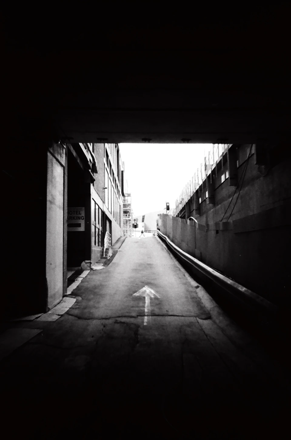 Narrow alleyway with concrete overpass arching over it in black and white tones