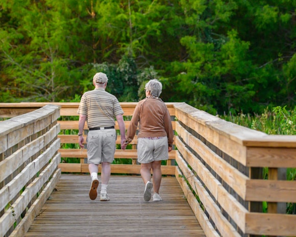 An elderly couple walking hand in hand along a forest trail, embodying vitality and longevity.