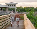A caregiver and senior woman walking hand in hand in a peaceful garden with blue and gold accents.