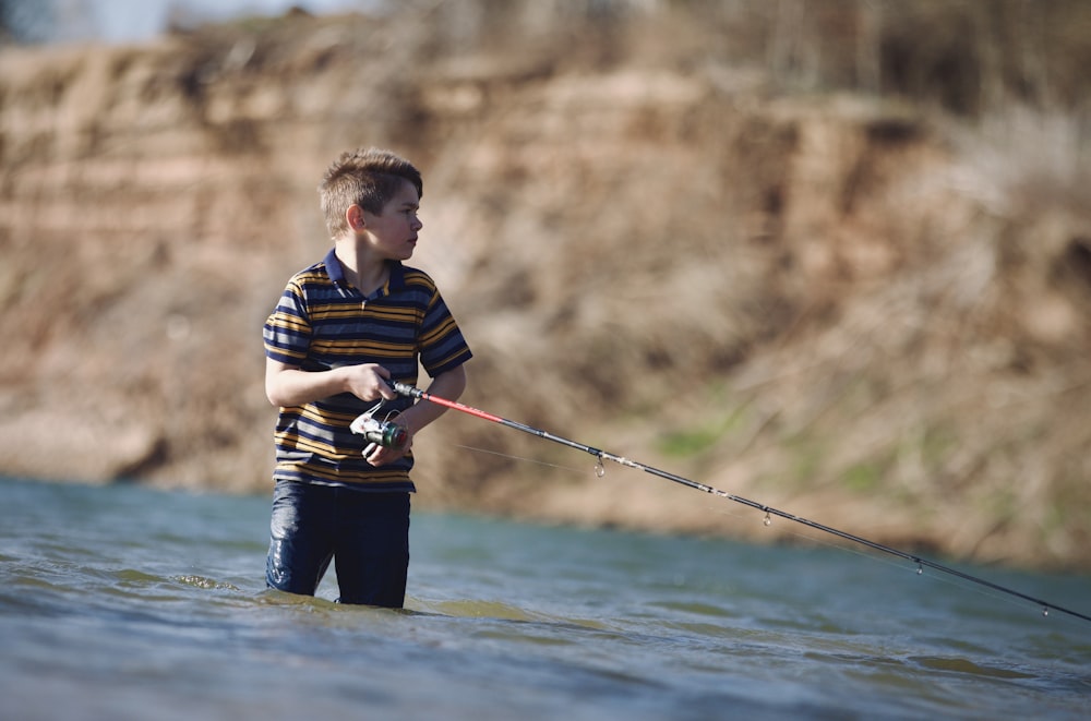 um menino em pé na água segurando uma vara de pesca