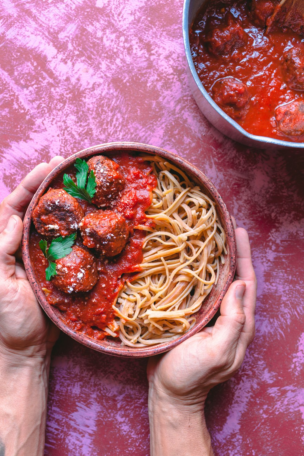 two hands holding a bowl of spaghetti and meatballs
