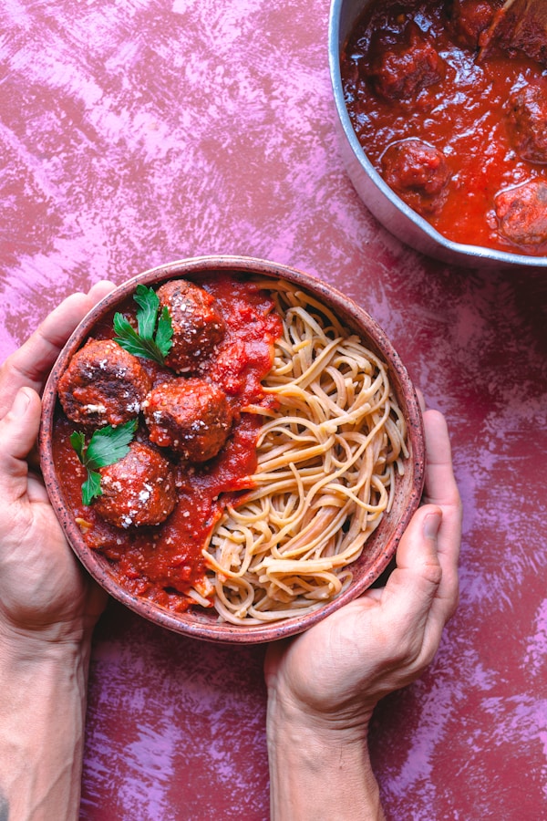 Two hands holding a bowl of spaghetti and meatballs