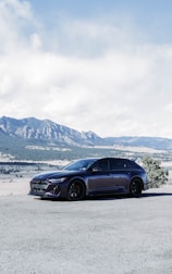 A shiny rental car parked in front of a scenic mountain view.